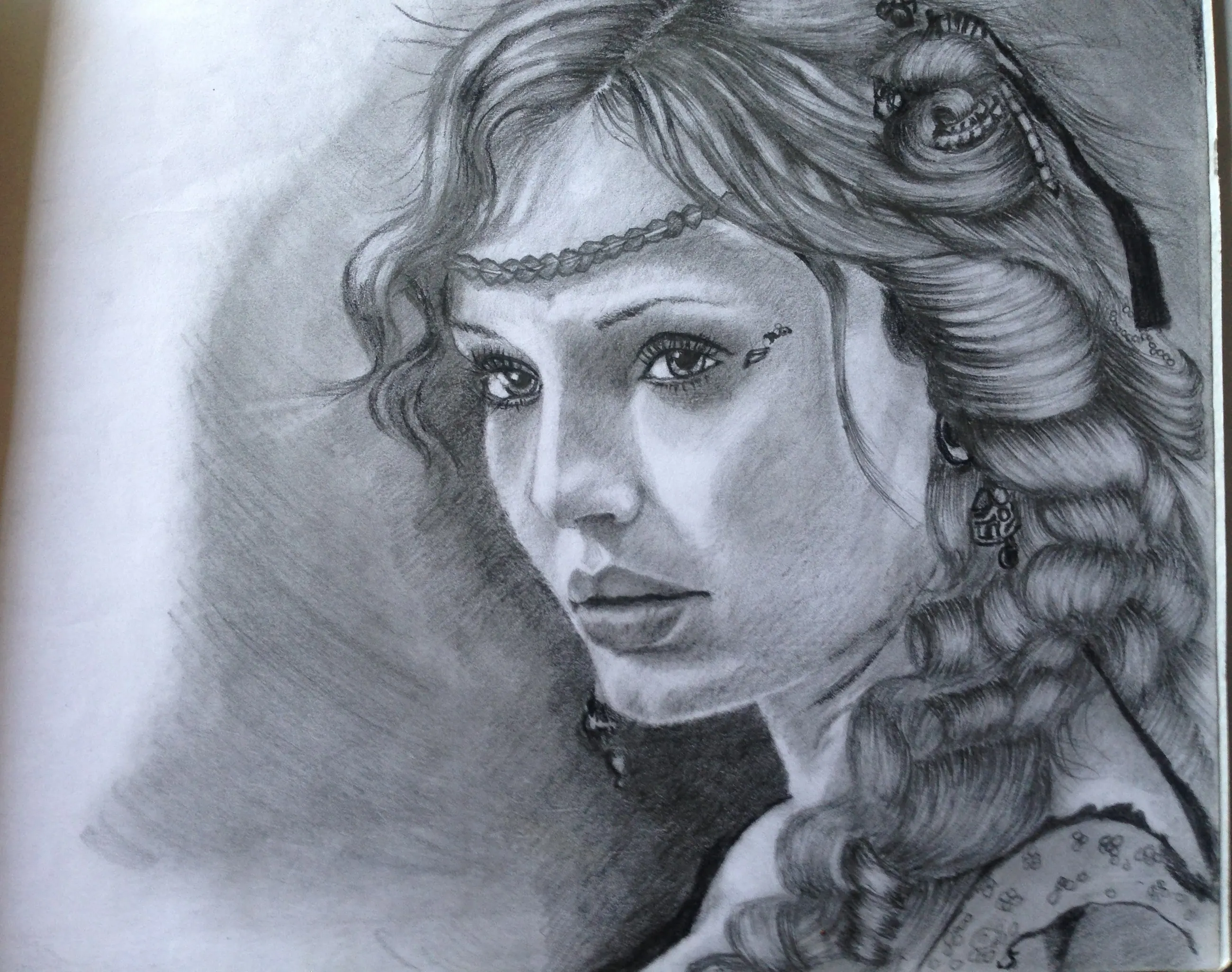 Graphite pencil drawing of a young woman with a beaded circlet across her forehead and long braided, curled hair, looking at the viewer over her shoulder, photographed on a sketchbook page.